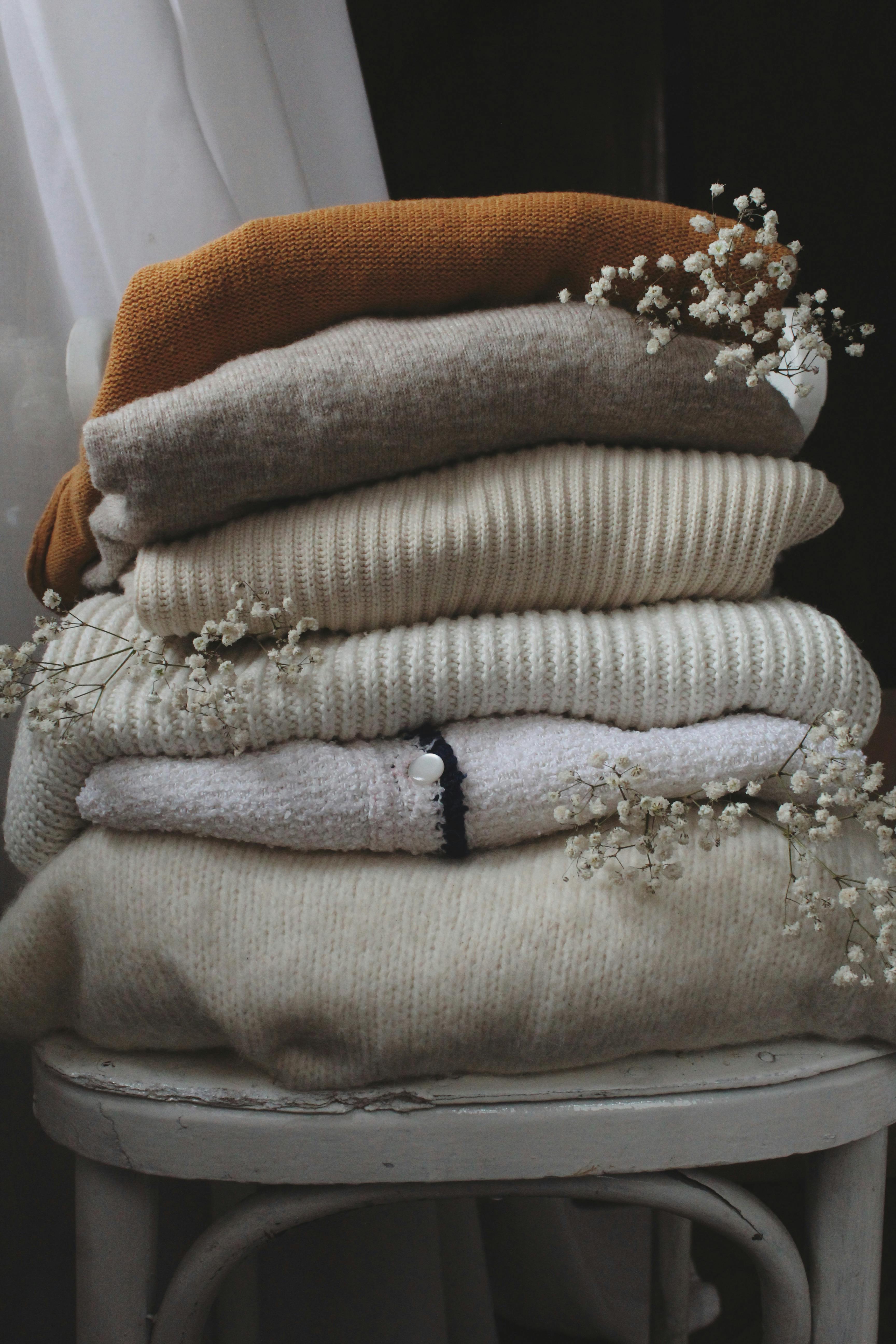 Pile of neutral colored sweaters arranged beautifully with flowers curated by Styled After.