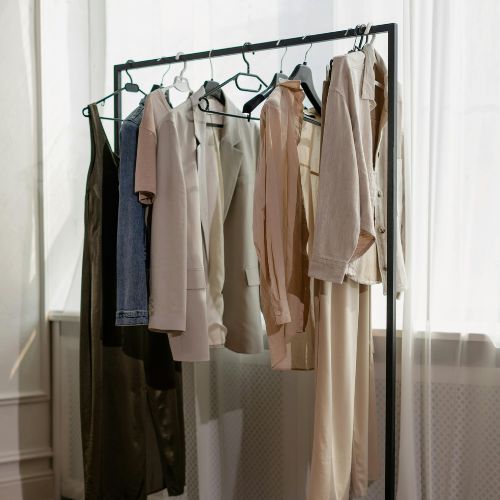 Elegant capsule wardrobe in neutral colors hanging on a rack curated by Styled After.