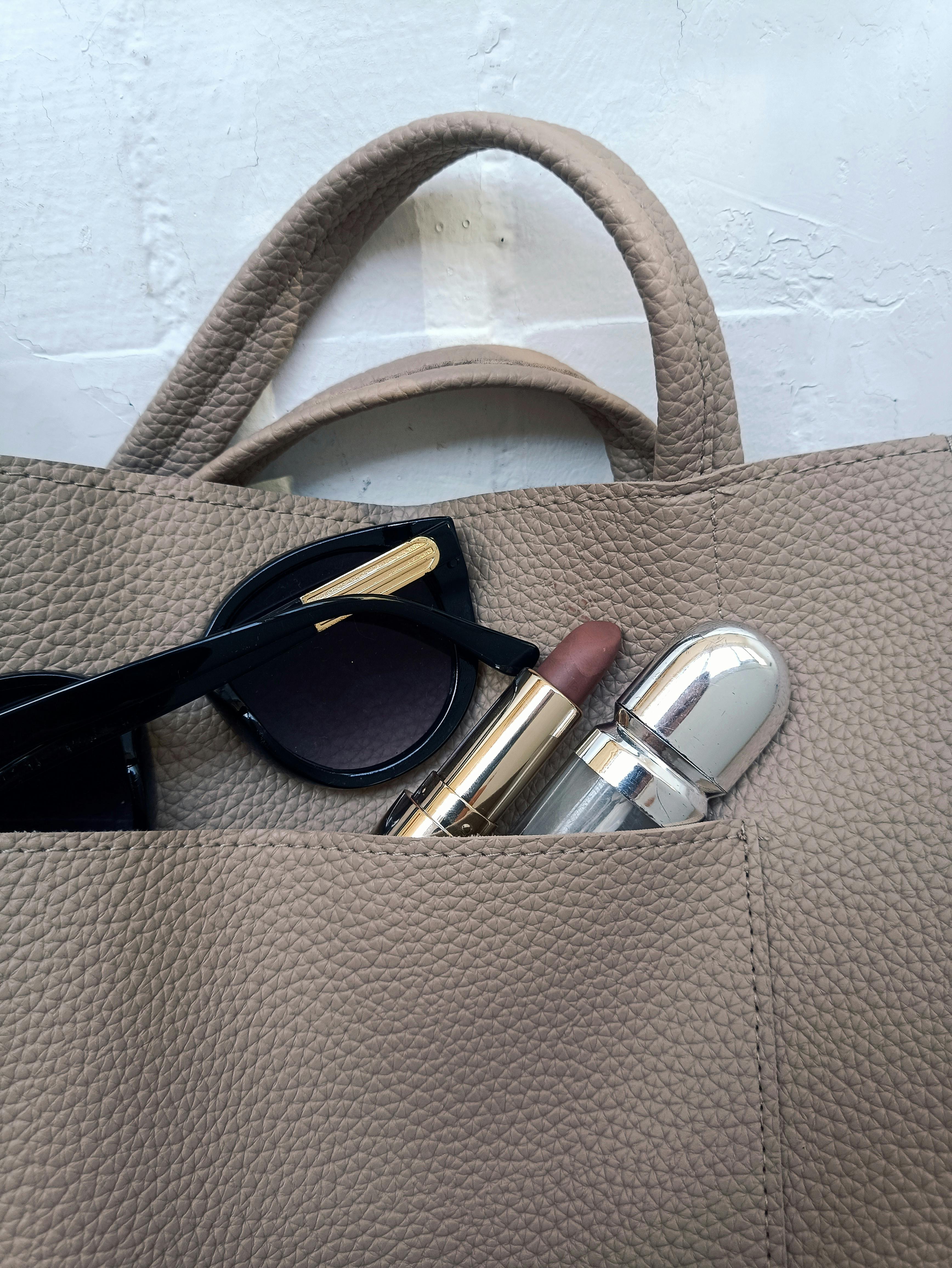 Pebbled leather, stone colored tote with black sunglasses and luxurious essentials, inspired by Seema Patel in And Just Like That, curated by Styled After.
